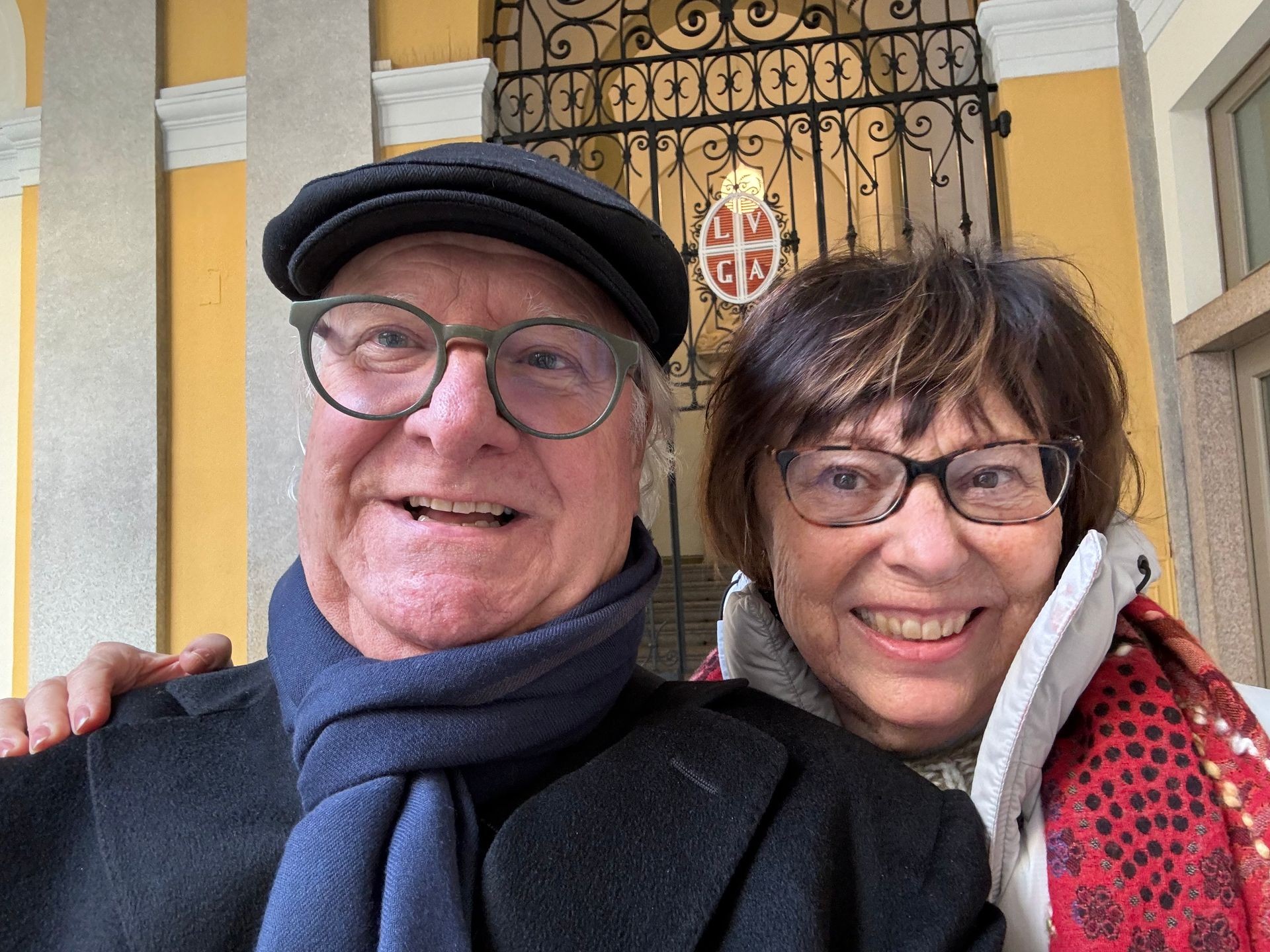 Smiling man and woman wearing glasses posing in front of ornate gate.